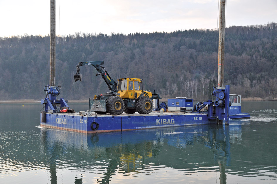 Schweiz: Mit dem Skidder auf dem Wasser. Holzernte auf dem Zürichsee, der Skidder arbeitet von einem Floß aus. 